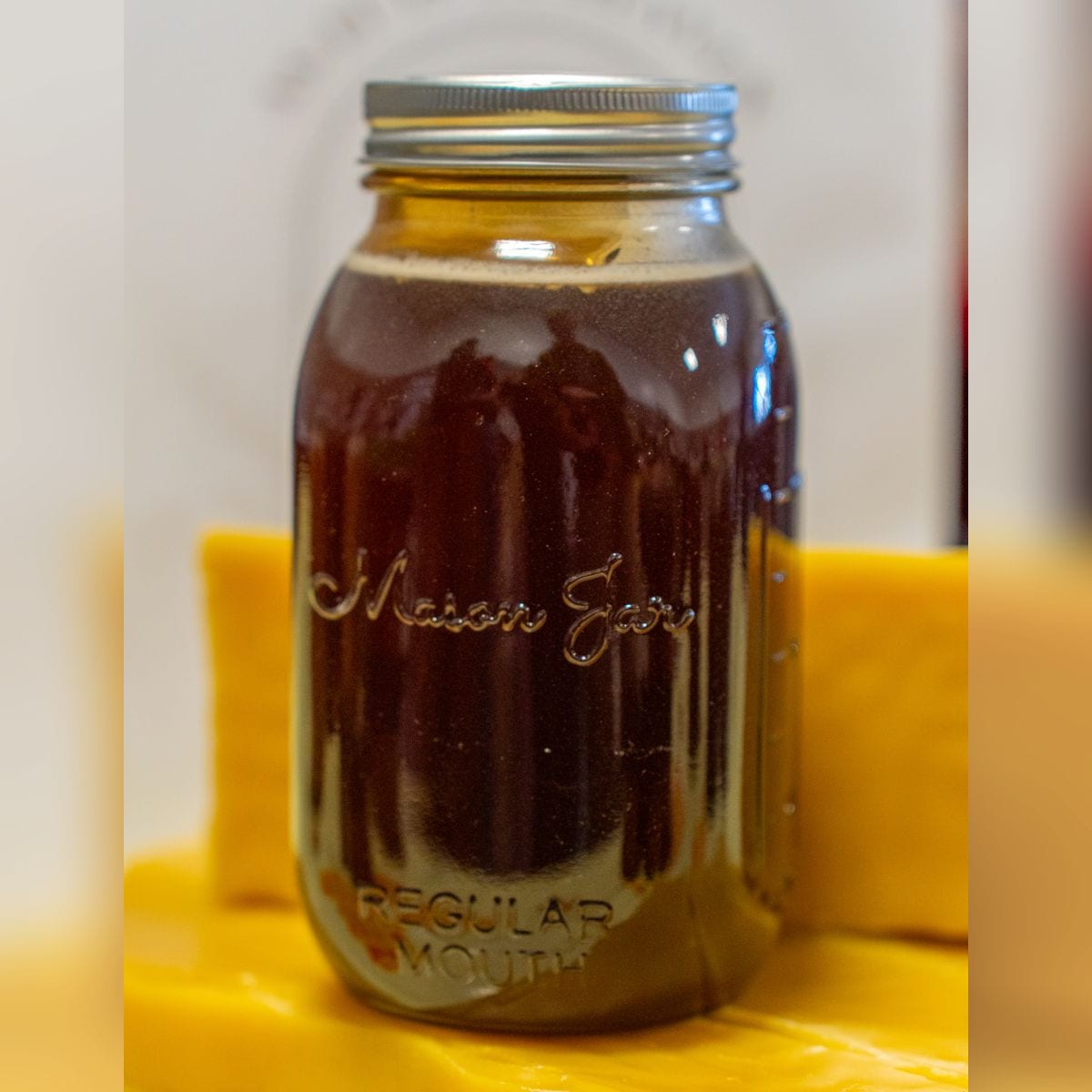 A quart mason jar filled with dark honey, standing on a slab of beeswax