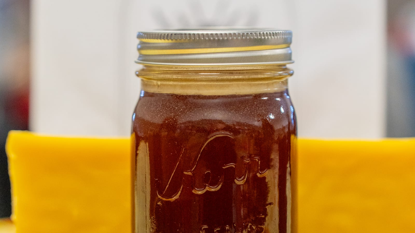 A Kerr mason quart of dark honey standing on a thick slab of golden beeswax on a market table