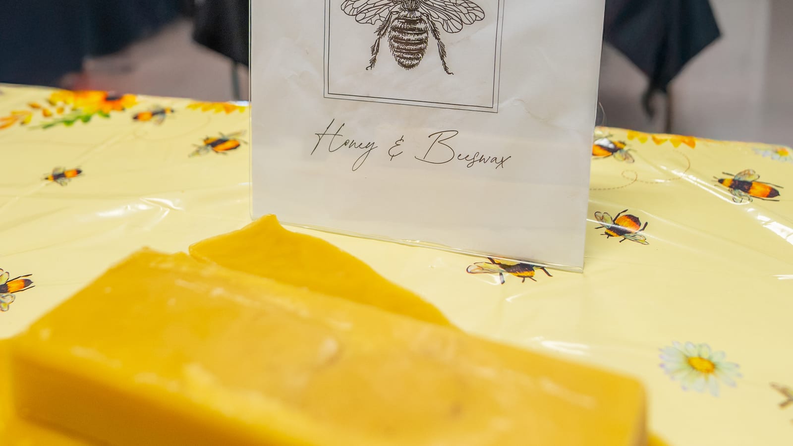 A paper bag printed Honey and Beeswax standing on a market table beside a thick poured slab of golden wax