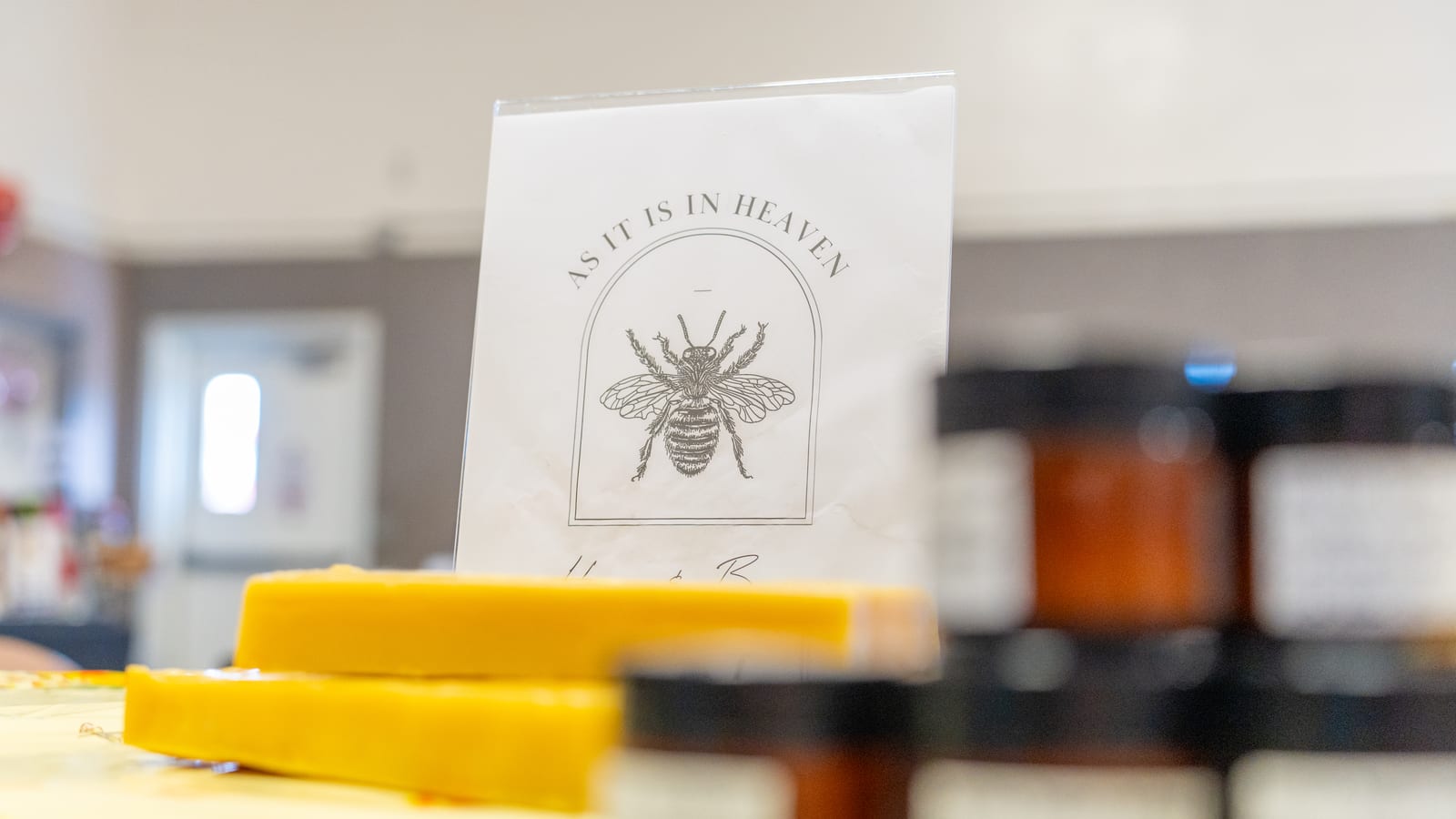 A row of poured beeswax slabs on a market table in front of the As It Is In Heaven sign