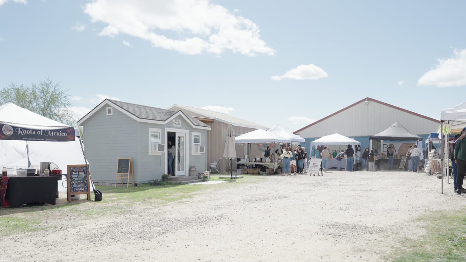 A row of white market tents down a gravel lane on a bright spring morning