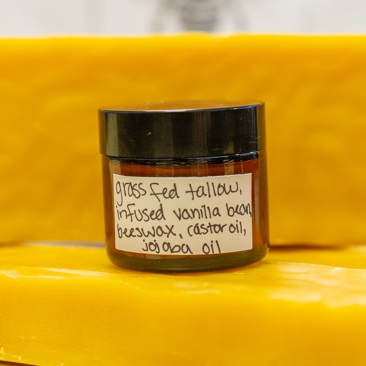 An amber glass jar of whipped tallow lotion on a slab of beeswax, hand-labelled grass fed tallow, infused vanilla bean, beeswax, castor oil, jojoba oil
